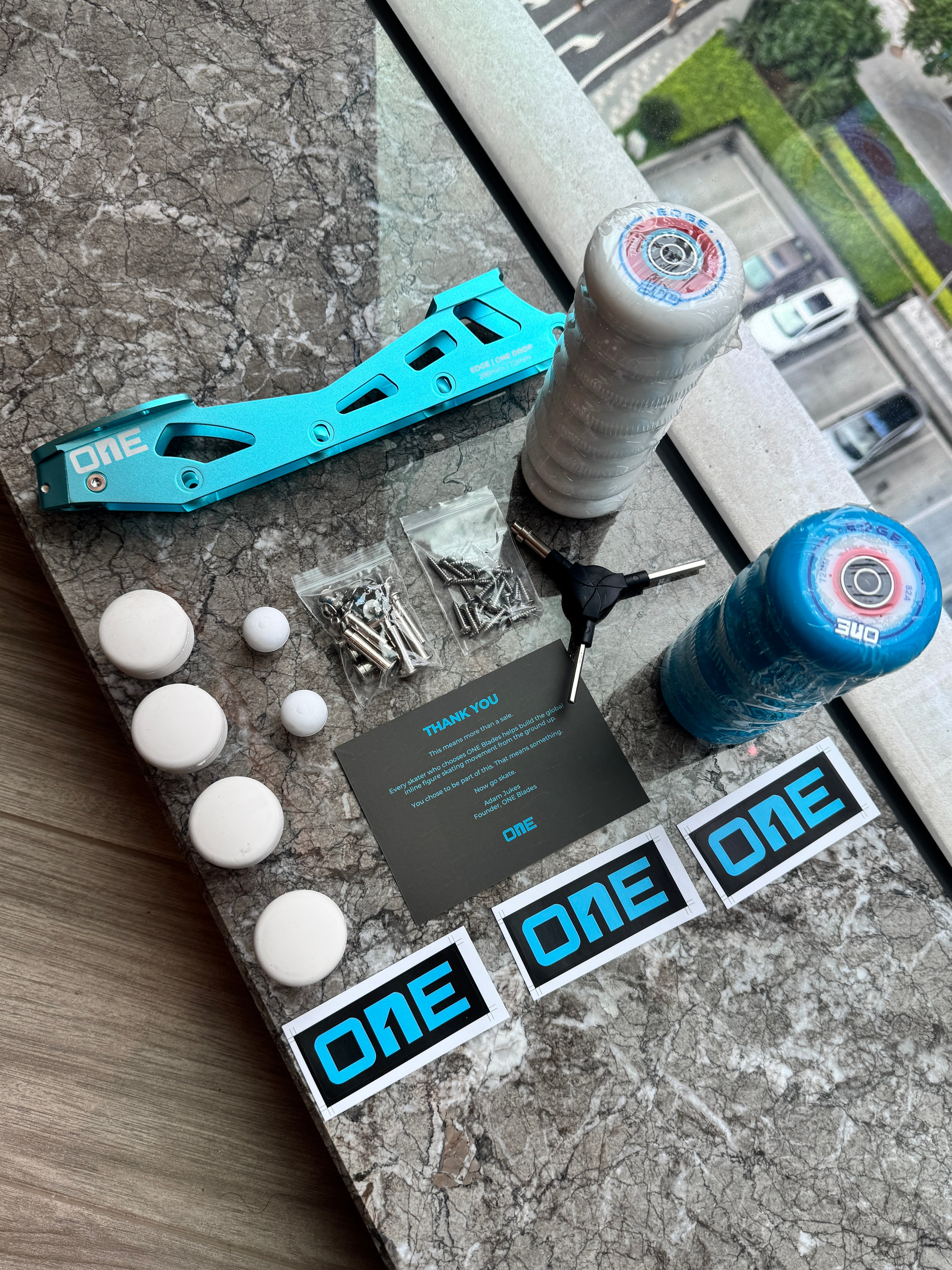 Blue inline figure skating parts and accessories on a concrete surface with 'ONE' branding.